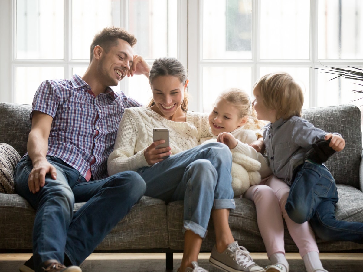 Eine junge Familie sitzt auf dem Sofa, die Mutter hält das Handy in der Hand und ist begeistert von der smartCon Steuerung